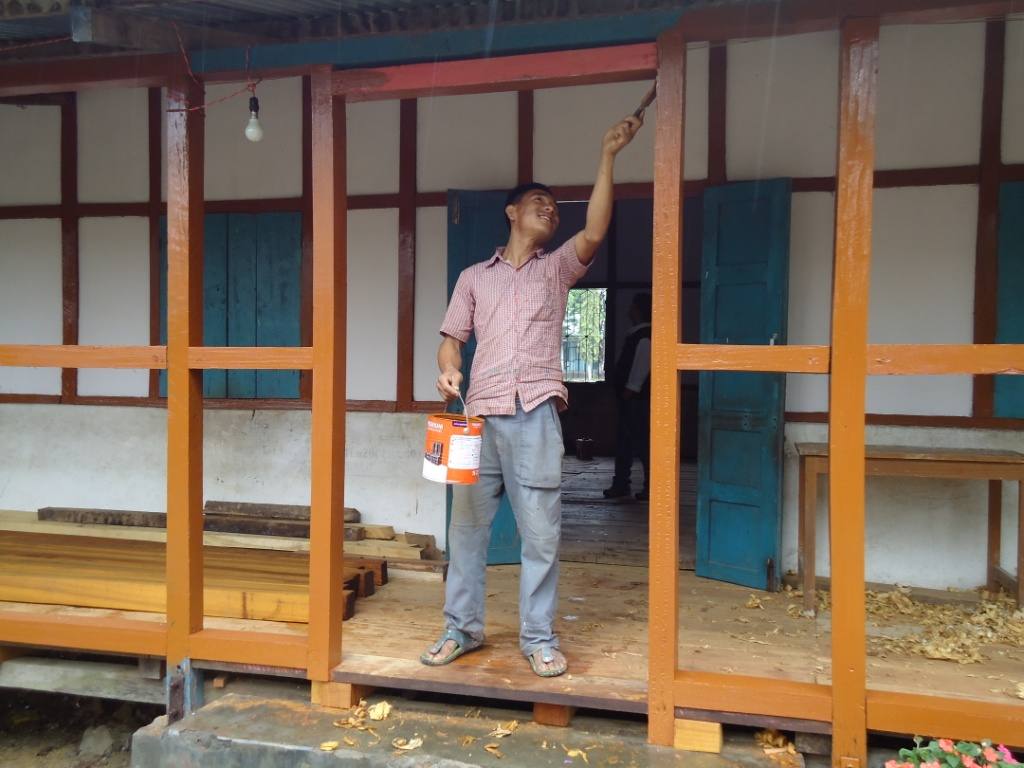 Mann streicht Holz auf der Terrasse der erweiterten Zahnklinik in Miao